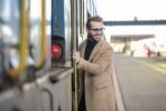 homme portant des lunettes un pull col roulé noir et un manteau beige long